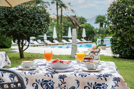 A table laid for breakfast with two glasses of orange juice looking out into a garden with a pool